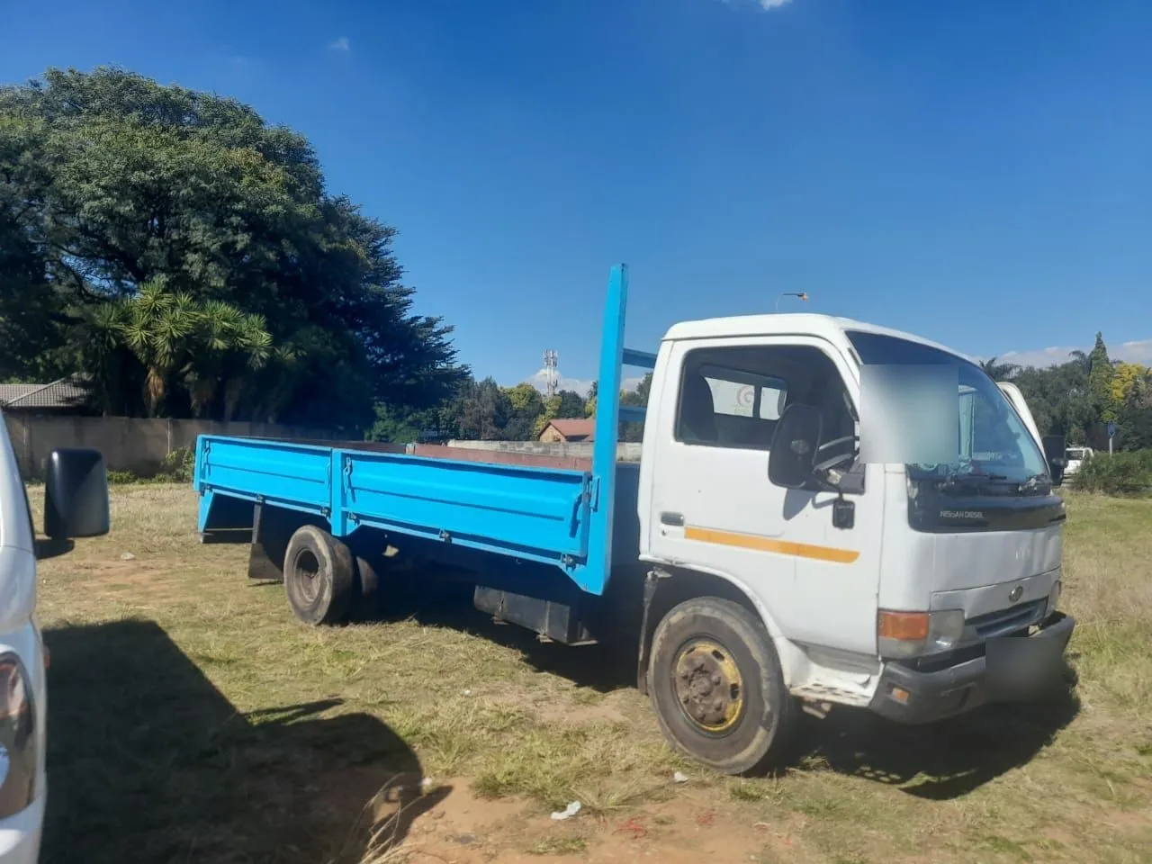 White-cab truck with an empty blue dropside deck parked on grass