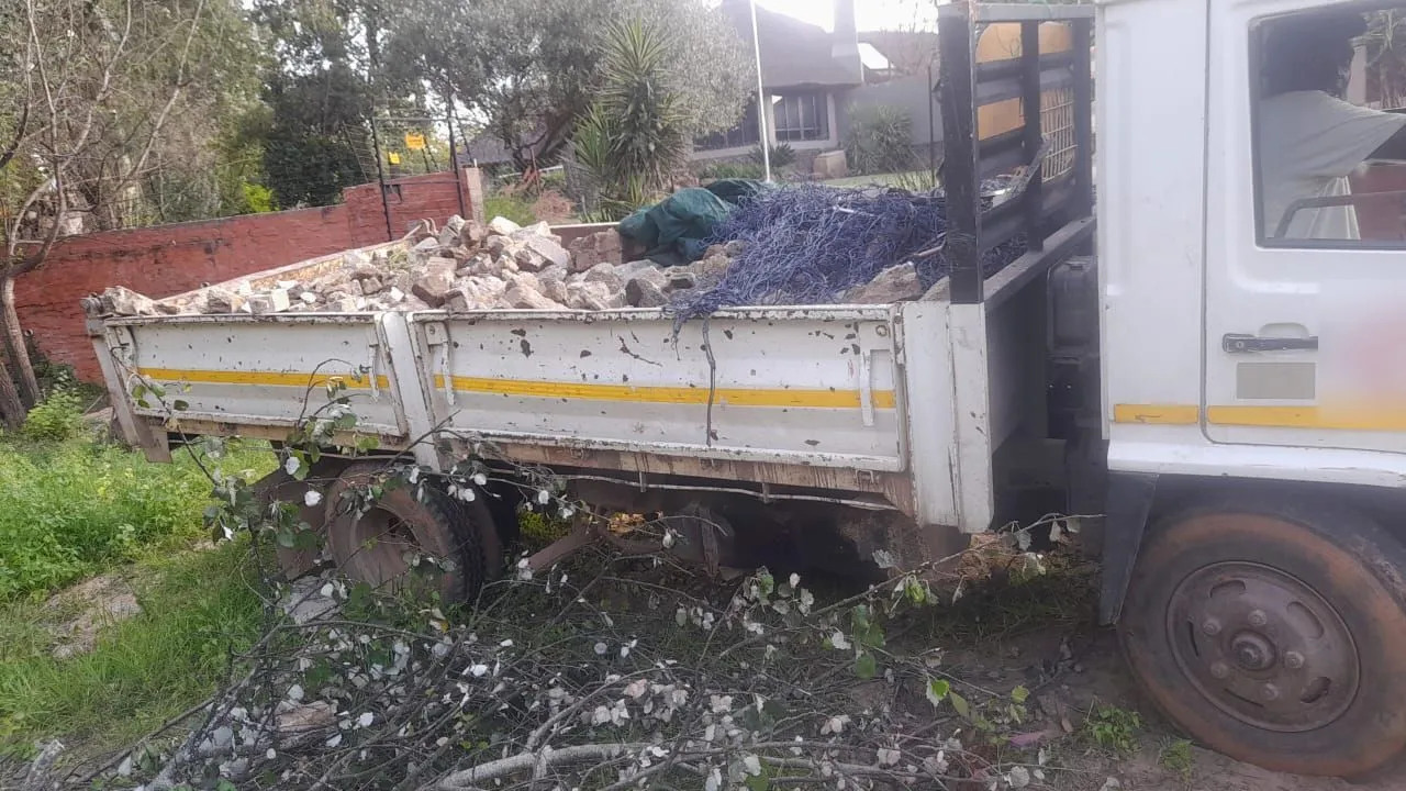 Truck loaded with broken bricks, a green tarp and blue netting beside a face-brick garden wall