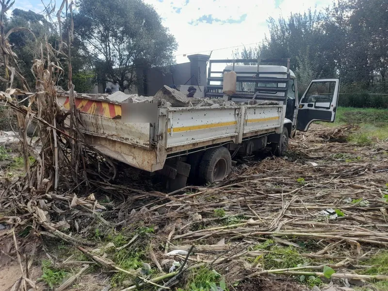 Dropside truck loaded with broken concrete and rock, parked on a plot cleared of dry maize stalks